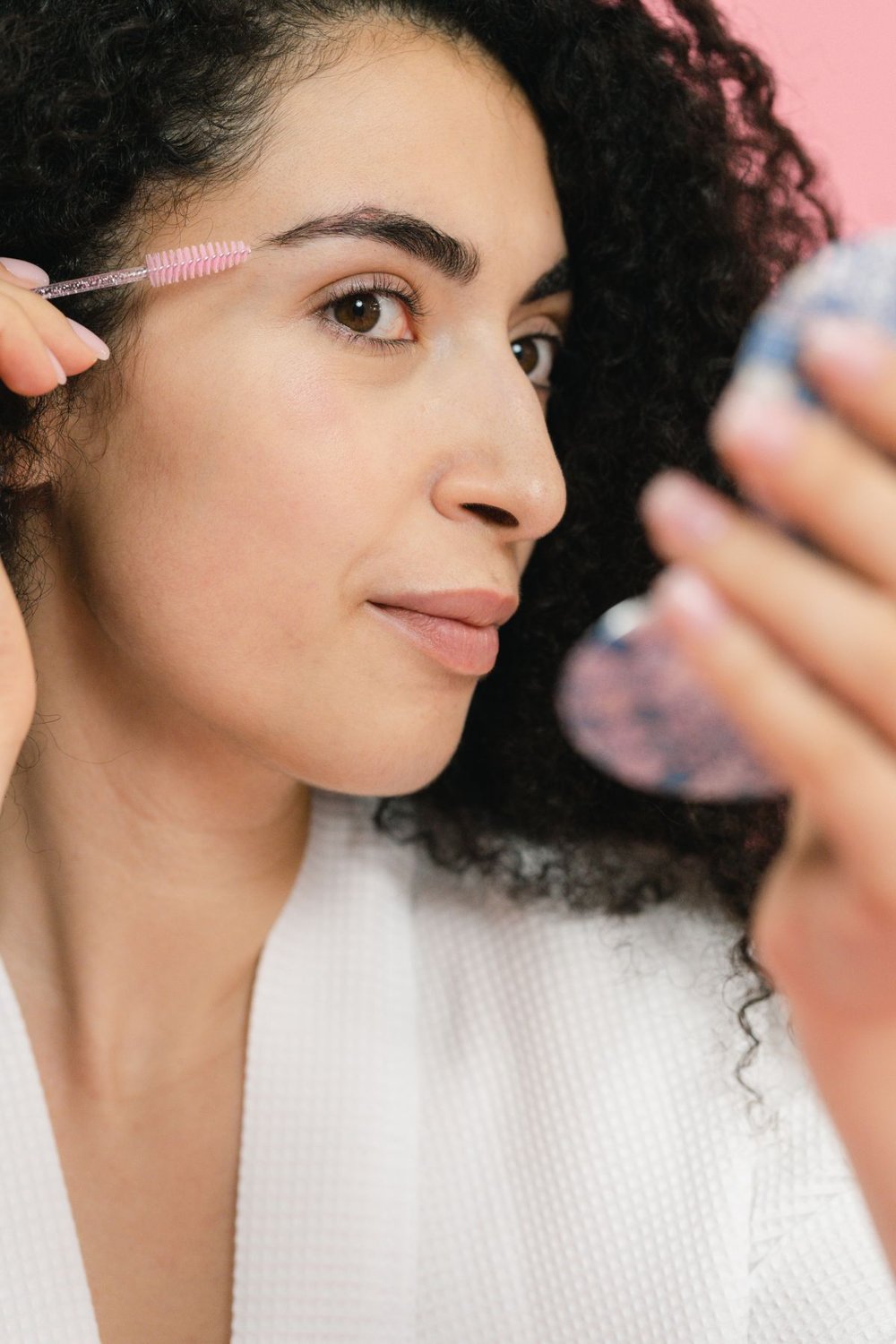Woman brushing her eyebrows while holding a mirror