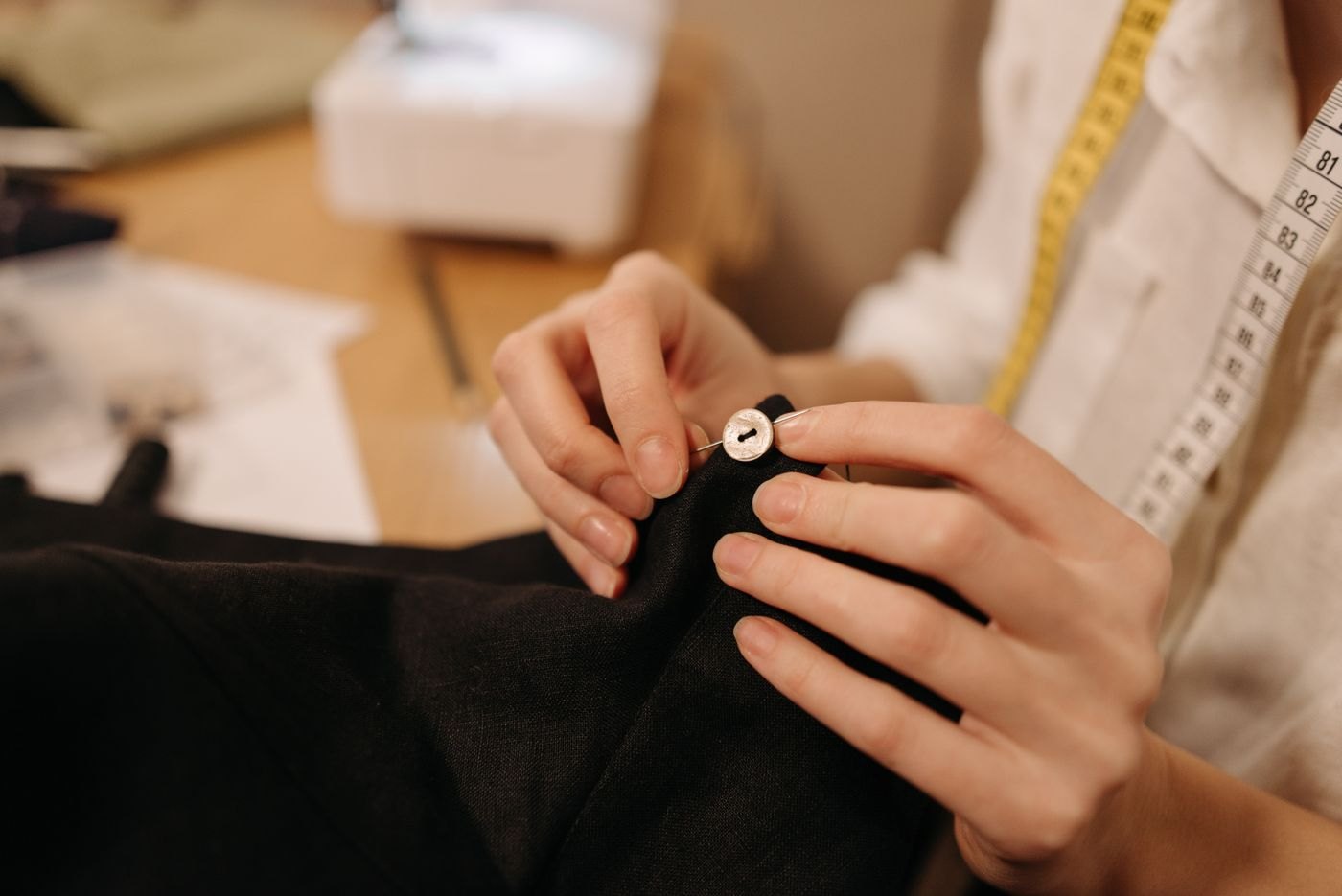 Hands sewing a button onto dark fabric