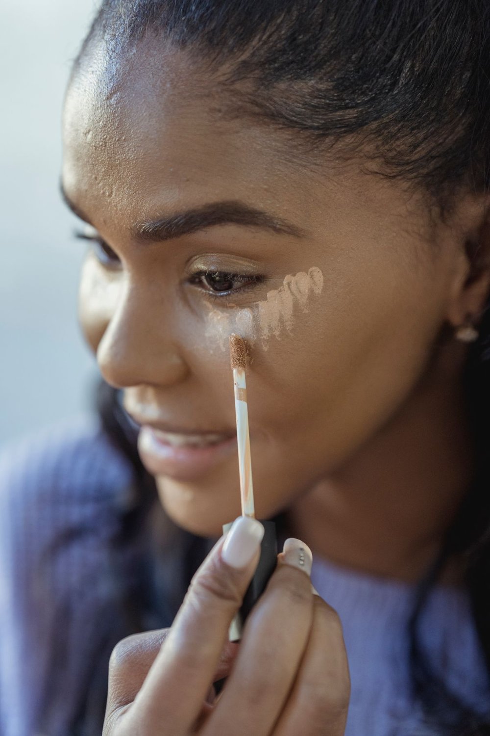 Woman applying concealer beneath one eye