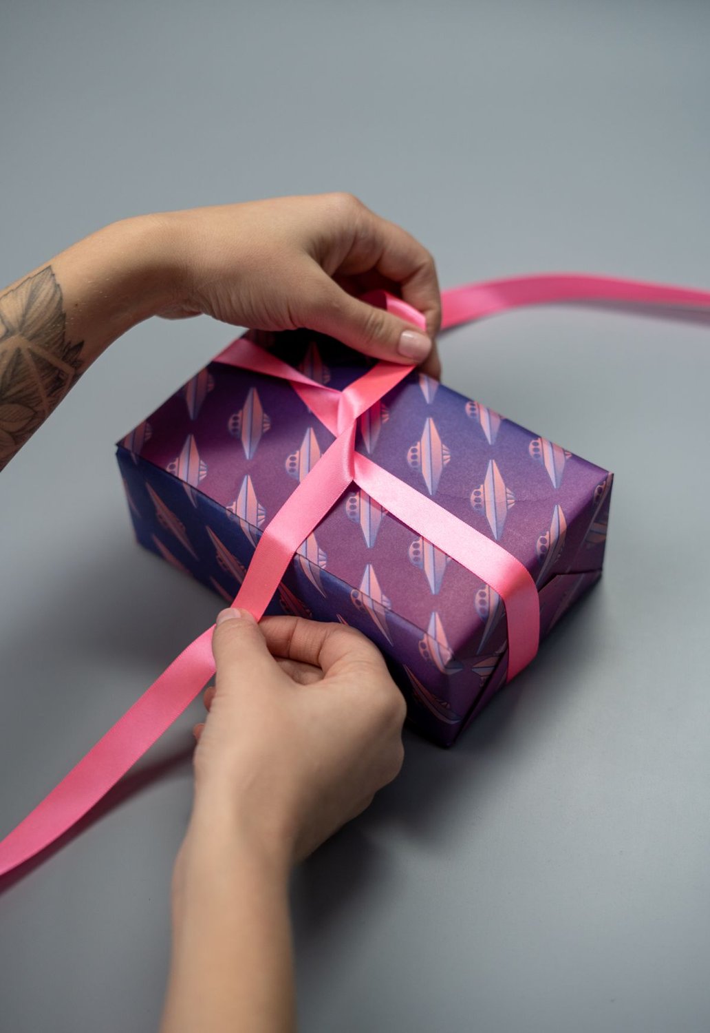 Hands wrapping a gift box with a pink ribbon