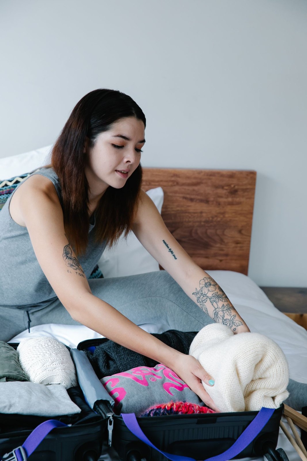 Woman folding clothes beside luggage on a bed