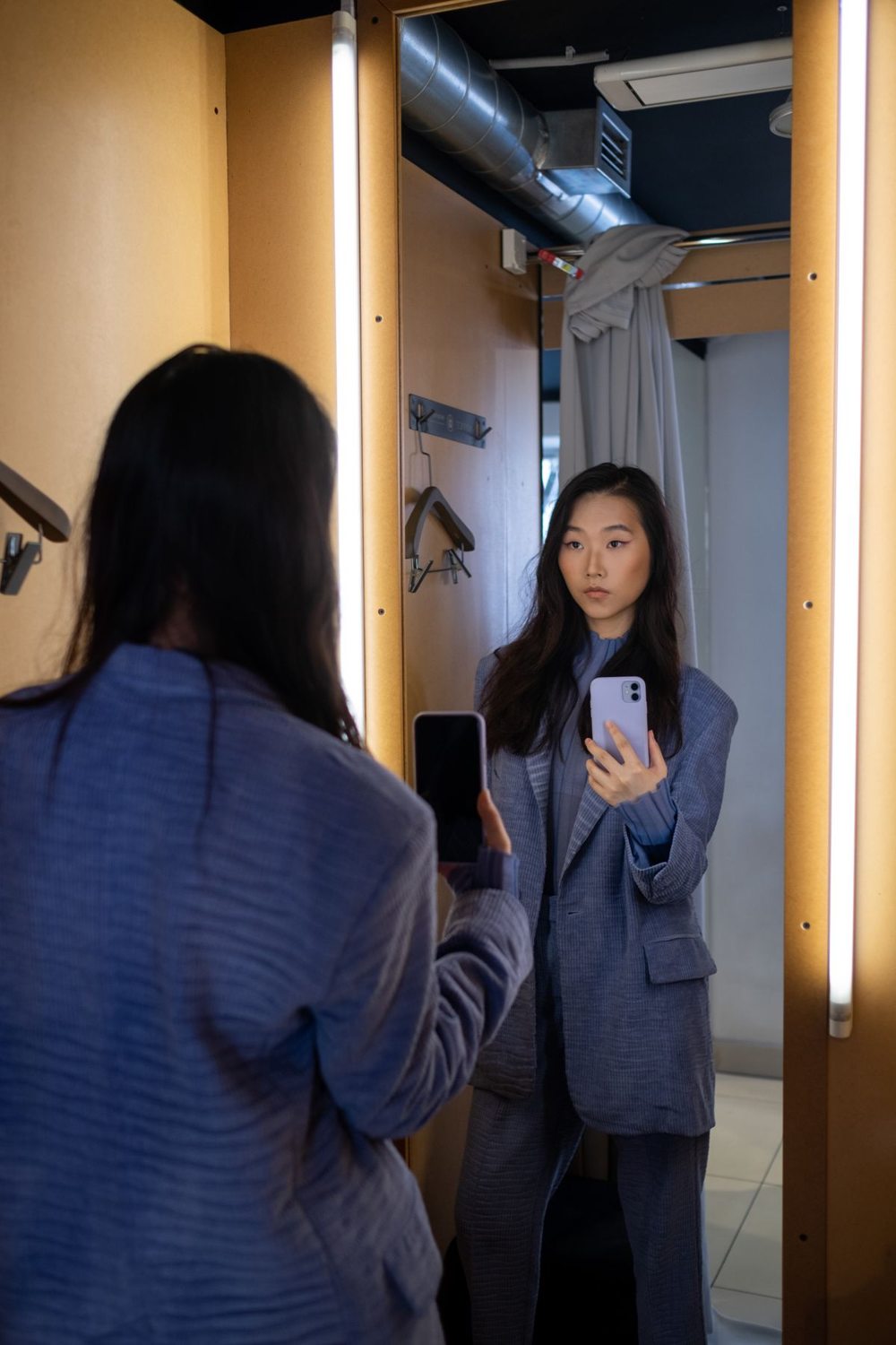 Woman photographing a blue blazer outfit in a fitting-room mirror