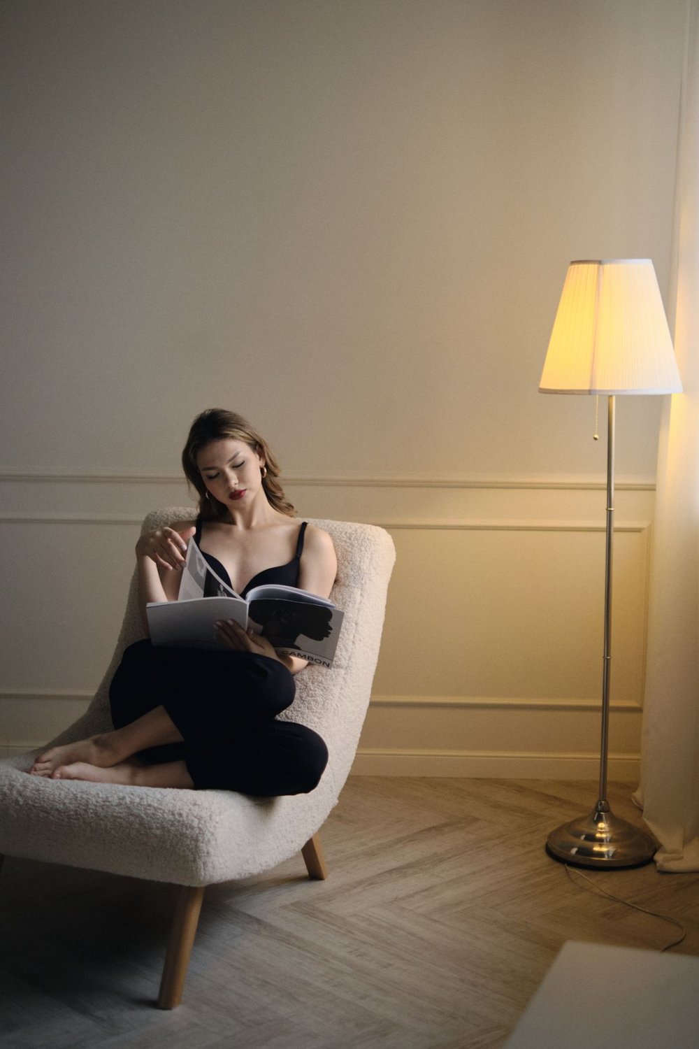 Woman reading in an armchair beside a floor lamp