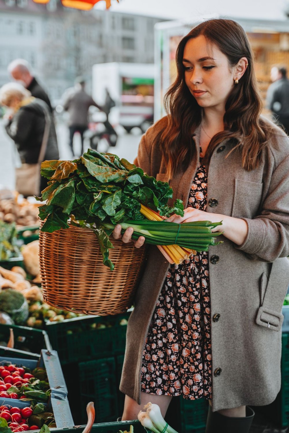 Woman with a woven basket choosing greens at an outdoor market